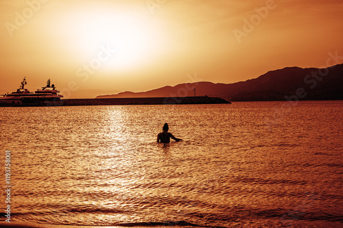 Obraz na płótnie Beautiful sunset with red colors on the sea with a girl in the water turned towards the low sun on the horizon w salonie
