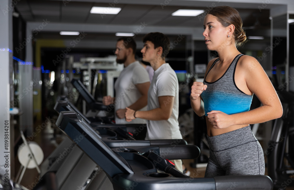 Focused girl works out with treadmill during class at fitness club. Gym visitor performs exercise, creates load on muscles. Athlete creates strong and attractive body through physical activity Focused girl works out with treadmill during class at fitness club. Gym visitor performs exercise, creates load on muscles. Athlete creates strong and attractive body through physical activity