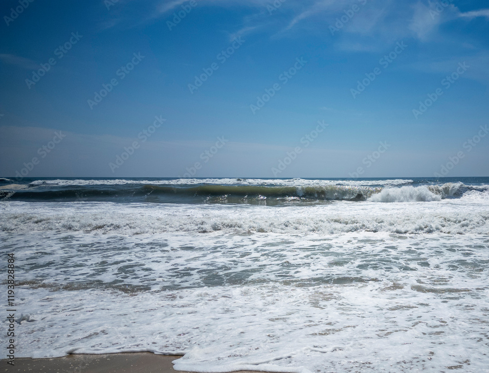 Fototapeta premium Waves Crashing on the Shoreline Under a Clear Blue Sky During Midday
