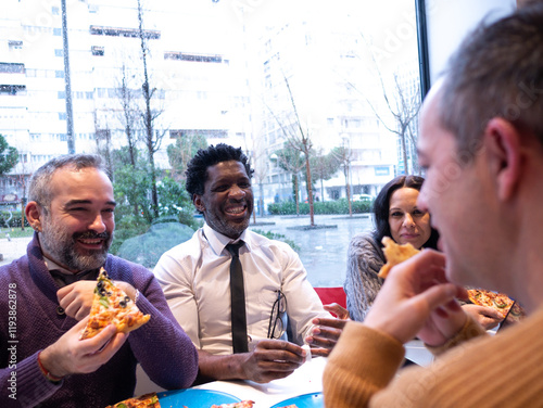 From the perspective of a man in a beige sweater, three colleagues with pizzas look at him while laughing. A phone is on the table, and rain falls outside the bright office window