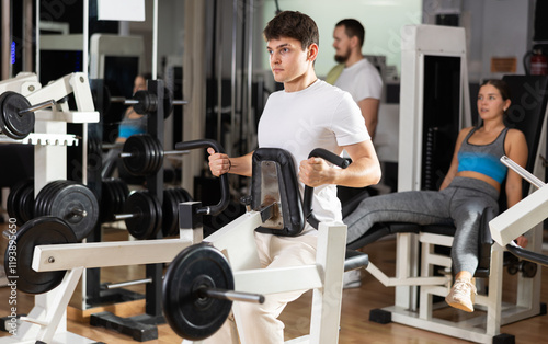 Young male gym coach uses fitness equipment to strengthen muscles of arms and upper torso, and does exercises in gym. Athlete creates strong and attractive body through physical activity photo