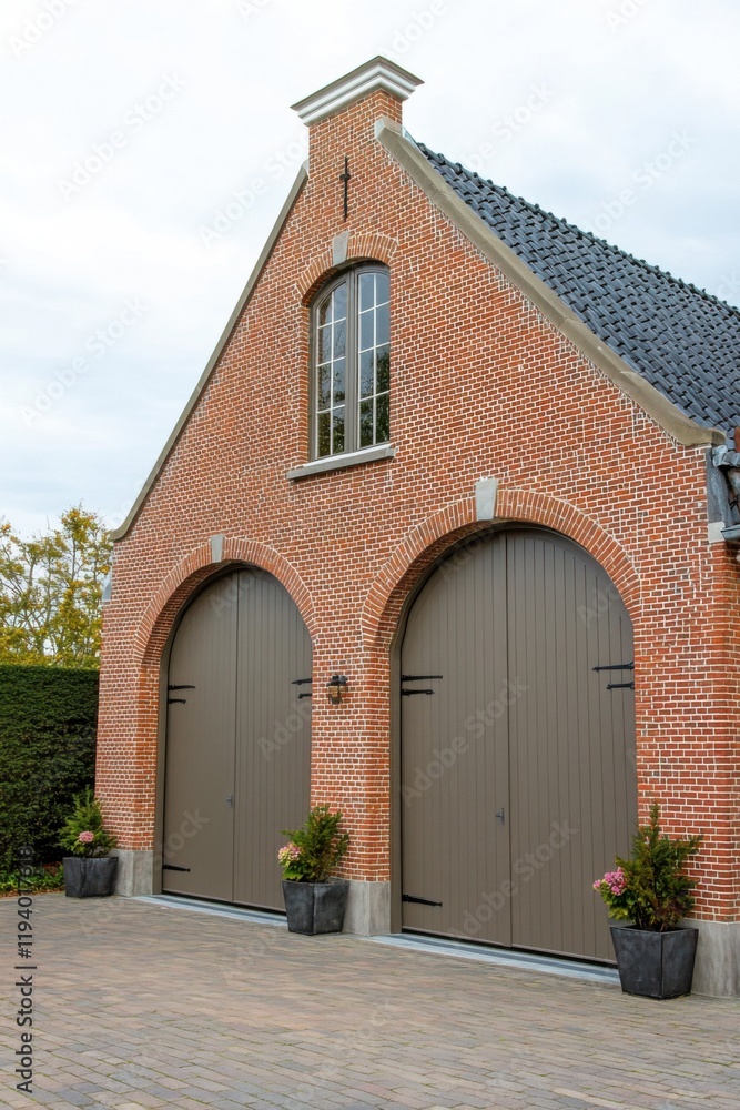 Classic brick barn with large wooden doors set in a serene garden landscape during a cloudy day Classic brick barn with large wooden doors set in a serene garden landscape during a cloudy day
