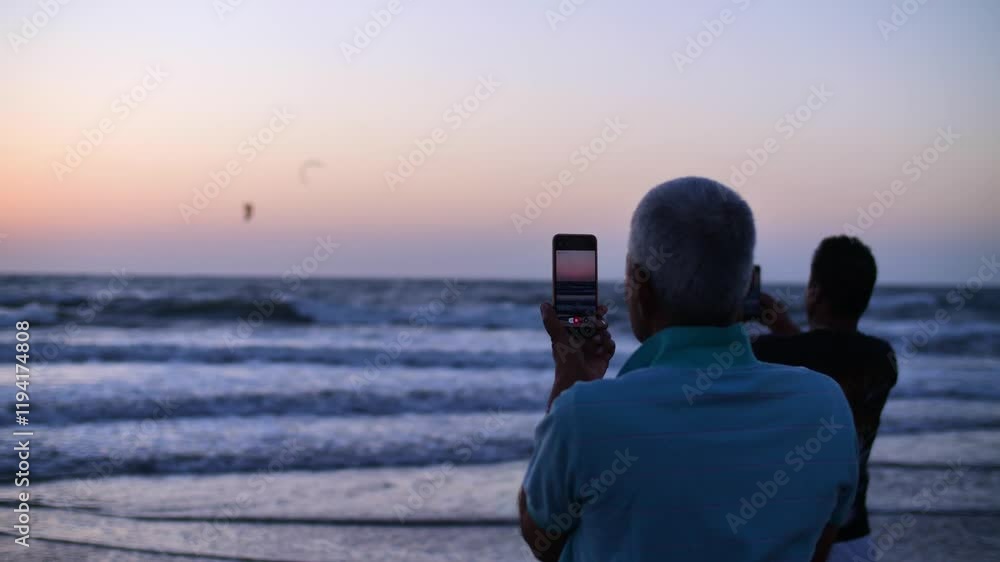 a mans films the sunset over the sea on his phone a mans films the sunset over the sea on his phone