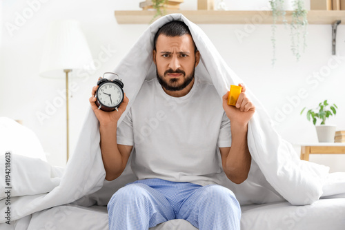 Stressed young man with alarm clock and pills in bedroom photo