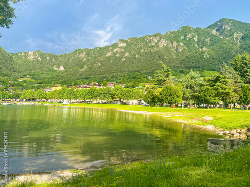 Stunning landscape featuring a calm lake reflecting the cloudy sky. Majestic mountains rise in the distance, framed by lush greenery, creating a tranquil and picturesque scene. Lake Idro, Crone, Italy photo