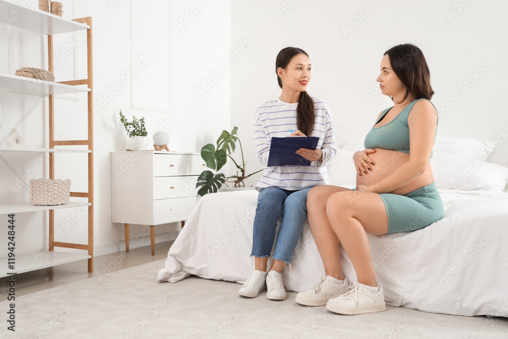 Young Asian doula with clipboard and pregnant woman sitting in bedroom Young Asian doula with clipboard and pregnant woman sitting in bedroom