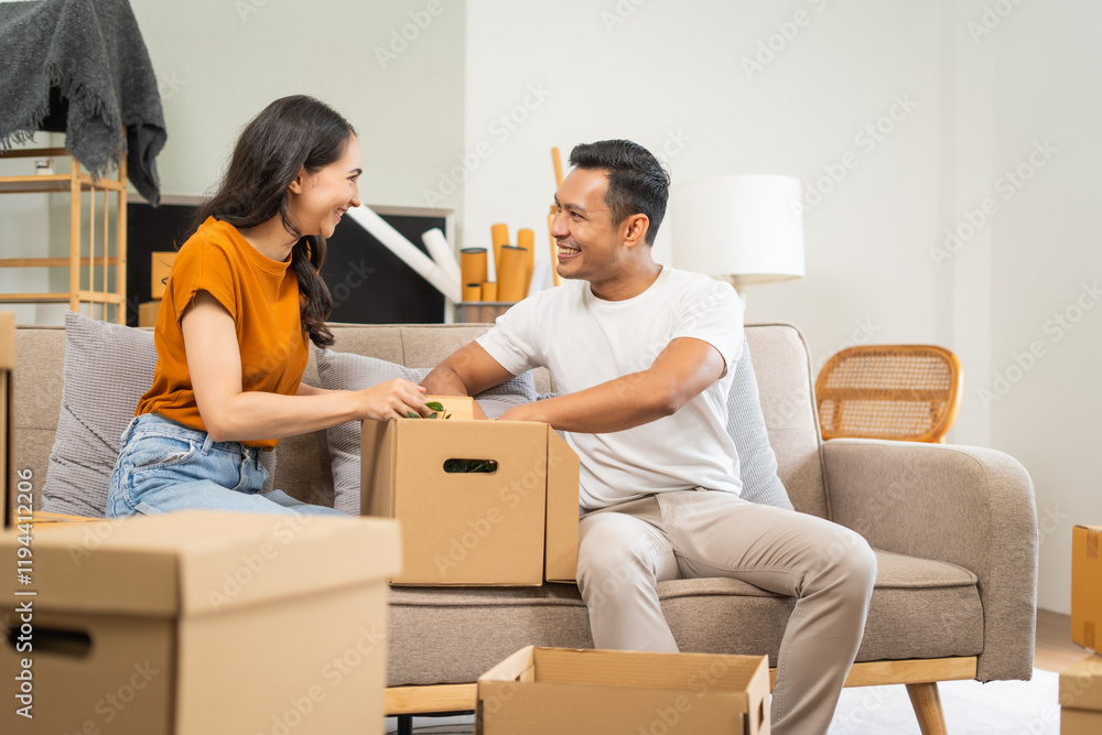 A happy young couple sits on a sofa, packing belongings into boxes, preparing to move to a new house, enjoying teamwork, organizing items, showing excitement, and embracing a fresh start A happy young couple sits on a sofa, packing belongings into boxes, preparing to move to a new house, enjoying teamwork, organizing items, showing excitement, and embracing a fresh start