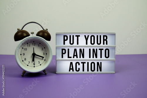 Put Your Plan Into Action text on light box with alarm clock on purple background photo