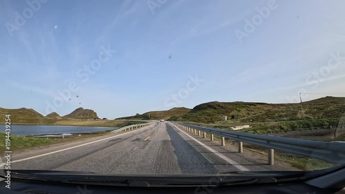 Driving through the tundra in northern Norway on E69 road. Surrounded by grassy hills with rocks and a scenic lake. A peaceful and remote landscape unfolds. photo