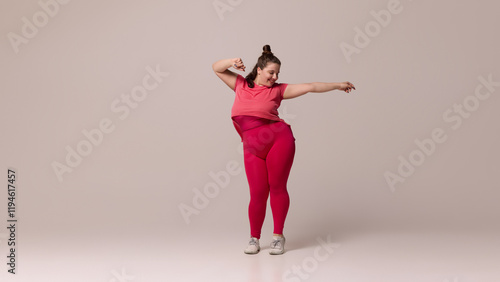 Smiling chubby woman dressed sportswear gracefully leaning with extended arm against white studio background. Fashion and style. Concept of beauty, fitness, movement, dance and music.