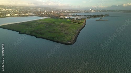 Aerial view of Cesar Chavez Park, a peninsula extending into the San Francisco Bay, featuring grassy hills, a shoreline, and the Berkeley cityscape in the distance under a cloudy sky photo