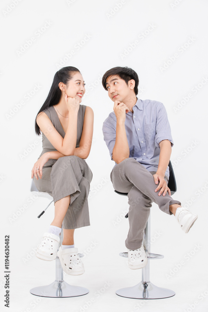 Fototapeta premium Portrait of lovely young asian happy attractive cheerful couple love, Joyful sweethearts enjoy good time romantic date, sitting on stools posing to camera smiling against together on white background.