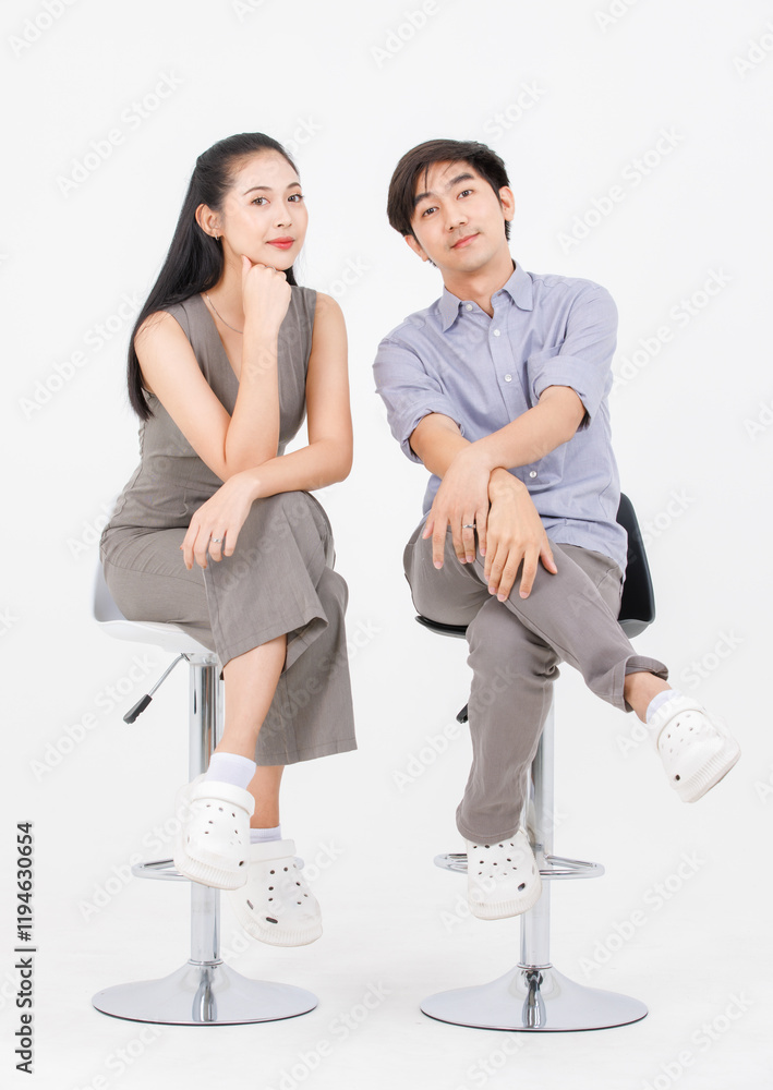 Fototapeta premium Portrait of lovely young asian happy attractive cheerful couple love, Joyful sweethearts enjoy good time romantic date, sitting on stools posing to camera smiling against together on white background.