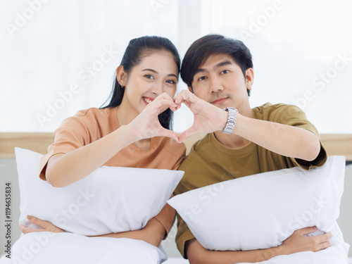 Obraz na plátne Portrait of young lovely sweet attractive asian happy couple love posing to camera smiling hugging pillow sitting on white bed in bedroom at home good time romantic together Valentine's day concept