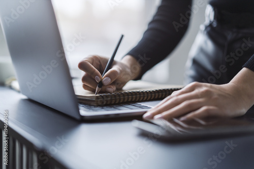 Close perspective of a woman's hand scribbling in a notepad on a stylish laptop, with a soft blur in the surroundings photo