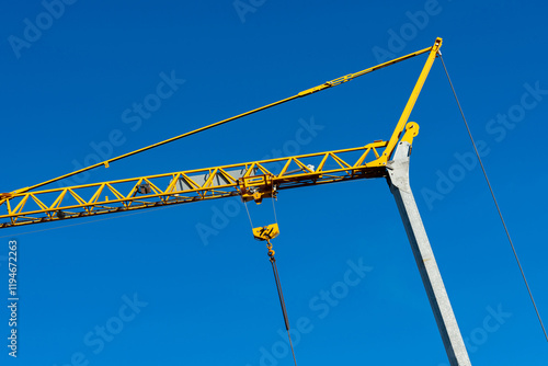 A tall construction crane reaches high above a clear blue sky, showcasing its yellow structure and strong cables. The crane is an essential tool for lifting heavy materials on construction sites. photo