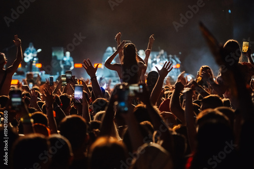 Crowd cheering and filming with smartphones at live music concert photo