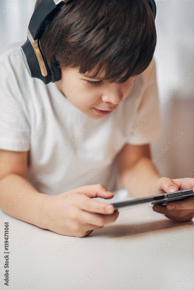 Cute boy with headphones playing games on his phone at home. Happy child looking at his smartphone. Cute boy with headphones playing games on his phone at home. Happy child looking at his smartphone.