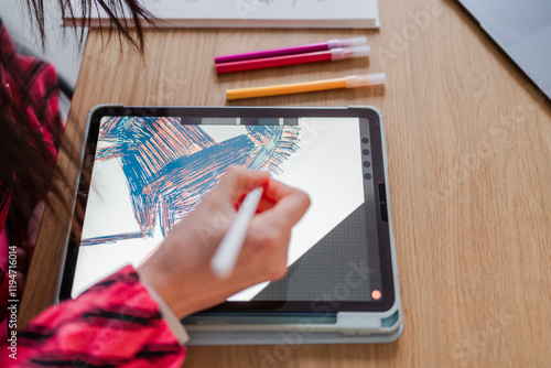 close-up view of a stylus creating colorful strokes on a tablet, with sketchbooks and markers nearby on a wooden desk in a modern studio workspace. photo