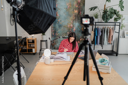 wide-angle view of a stylish studio setup showing a digital artist at a desk with sketchbooks, a tablet, a microphone, and professional lighting equipment. photo