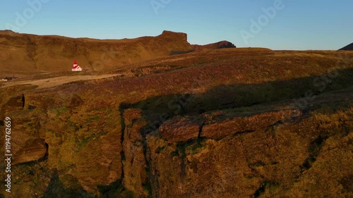 Wallpaper Mural A charming Icelandic scene capturing a small white church with a red roof, surrounded by rolling hills and rocky cliffs bathed in the warm glow of the morning sun. A peaceful rural setting. Torontodigital.ca