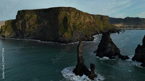 Stunning coastal view of Dyrhólaey cliffs with sea stacks along the black sand beach of Iceland. Unique rock formations with waves crashing against the shore, showcasing the natural beauty.
