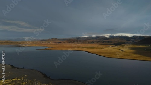 A peaceful Icelandic lake surrounded by rolling hills, with a stunning view of snow-capped mountains in the distance, capturing the beauty of Iceland’s serene landscapes.