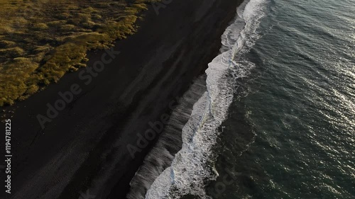 A stunning aerial shot of the waves crashing on the contrasting black sand beach of Iceland, showcasing the blend of deep ocean blue and the natural black coastline.