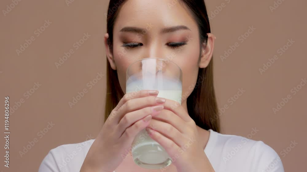 Happy young asian woman drinking a glass of milk or water on a solid background Happy young asian woman drinking a glass of milk or water on a solid background