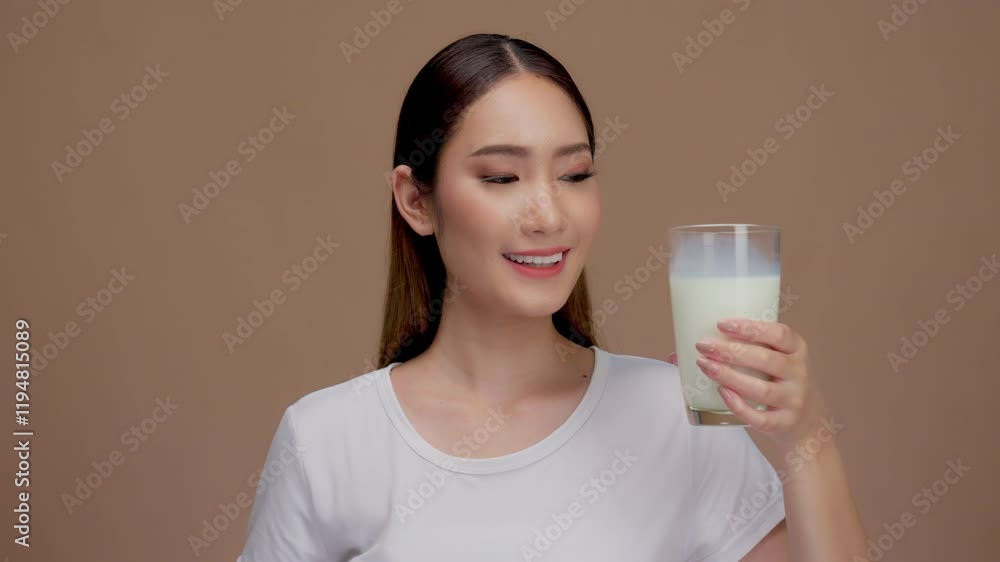 Happy young asian woman drinking a glass of milk or water on a solid background Happy young asian woman drinking a glass of milk or water on a solid background