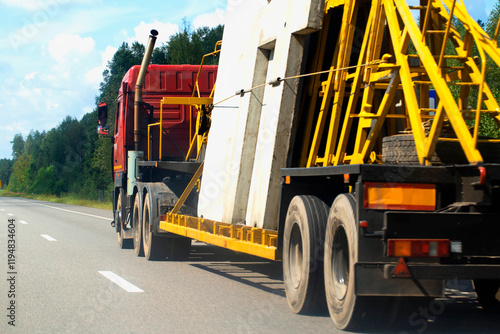 A panel truck with a semi-trailer transports reinforced concrete slabs for building a house. Cargo transportation in summer along the road against the backdrop of the forest. Copy space for text photo