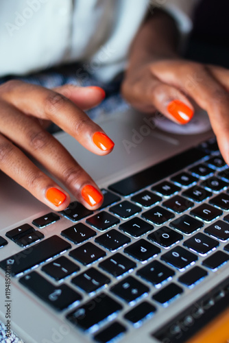 Cropped image of female's fingers with perfect orange nail polish over keyboard of netbook, woman freelancer yuping text on laptop computer pressing buttons for creating text indoors at home interior photo