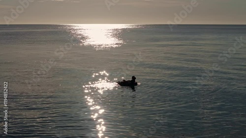 Two young friends float on an inflatable ring at Mabua Beach, silhouetted by the warm glow of the late afternoon sun, creating a serene and cinematic sunset scene. photo