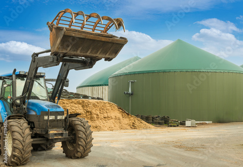 Tractor with a raised front loader in front of a biogas plant and maize chaff depot - 8795