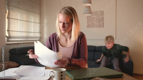 A mother works from home on her laptop in the living room, focused on her tasks, while her children play energetically in the background.