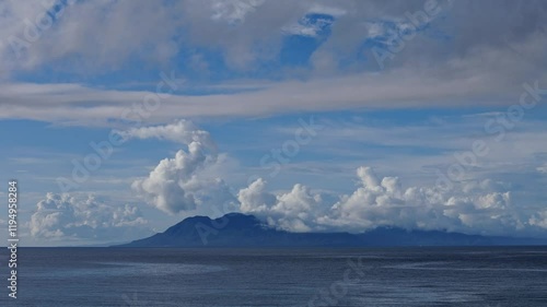 A breathtaking view across the Surigao Strait in the Philippines, showcasing calm blue waters and the distant islands of Leyte and Panaon silhouetted against a cloudy horizon. photo