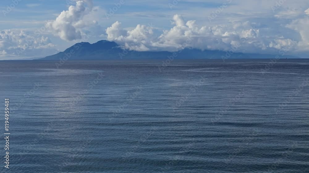 A tranquil view across the Surigao Strait's calm blue waters toward Panaon and Leyte, where the islands are silhouetted in clouds on the distant horizon under a sunny sky. A tranquil view across the Surigao Strait's calm blue waters toward Panaon and Leyte, where the islands are silhouetted in clouds on the distant horizon under a sunny sky.