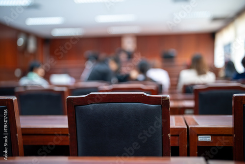 A classroom with a black chair in the foreground. The chair is empty and the room is filled with people