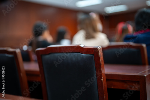 A group of people are sitting in a room with wooden chairs. The chairs are black and the room is dimly lit photo