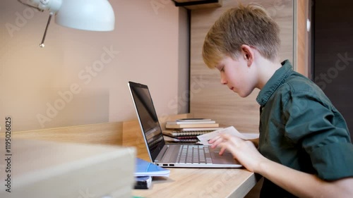 A teenage boy sits at his desk in his room, surrounded by books, notes and laptop, focusing on his studies