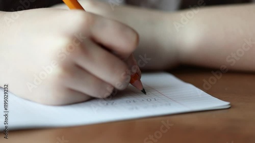 a child writes with a pencil and solves math examples in a checkered notebook. primary school education