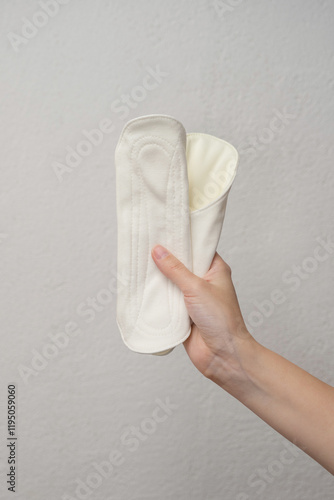 A woman's hand holding a sanitary pad on a gray background. Hygienic concept