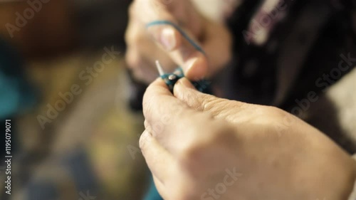 Elderly person knitting a blue scarf, sweater and hat in the living room of his house
