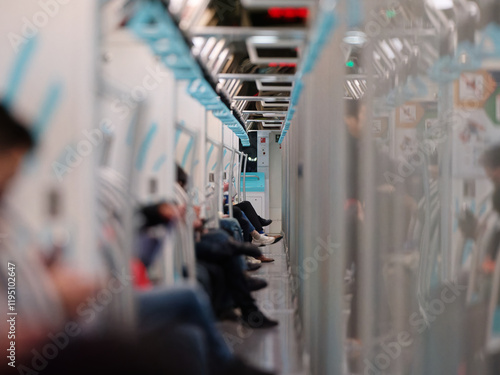 Crowd of passengers sitting with legs crossed on Urban Public Transport Metro. Asian people go to work by public transport. Focused on the far end of wall with blurry people.