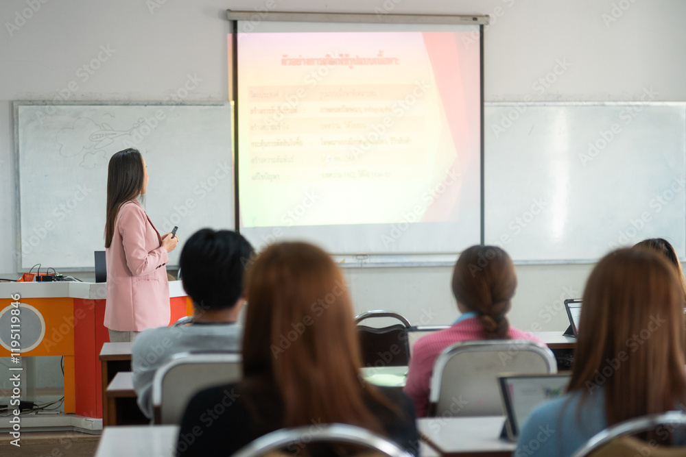 Fototapeta premium A lecturer stands at the front of the classroom, engaging students with a presentation projected on the screen. The students sit at desks, focused on the lecture.