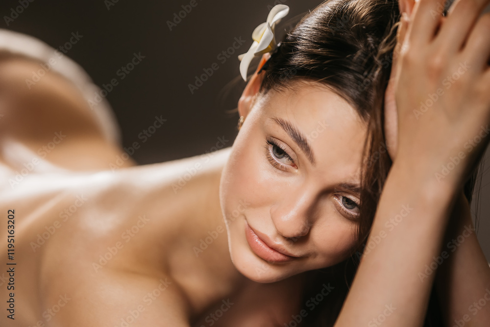 Fototapeta premium A beautiful young woman with smooth, flawless skin poses against a dark background. Perfect for spa, skincare, and beauty advertisements showcasing relaxation and self-care.