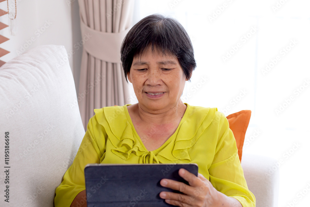 Senior asian woman waving during a video call on digital tablet sitting on sofa in living room at home, elderly video call online on tablet with distant sitting on couch, retirement and technology. Senior asian woman waving during a video call on digital tablet sitting on sofa in living room at home, elderly video call online on tablet with distant sitting on couch, retirement and technology.