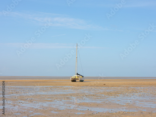 Fotografía Gestrandetes Segelboot bei Ebbe auf sandiger Wattlandschaft unter blauem Himmel