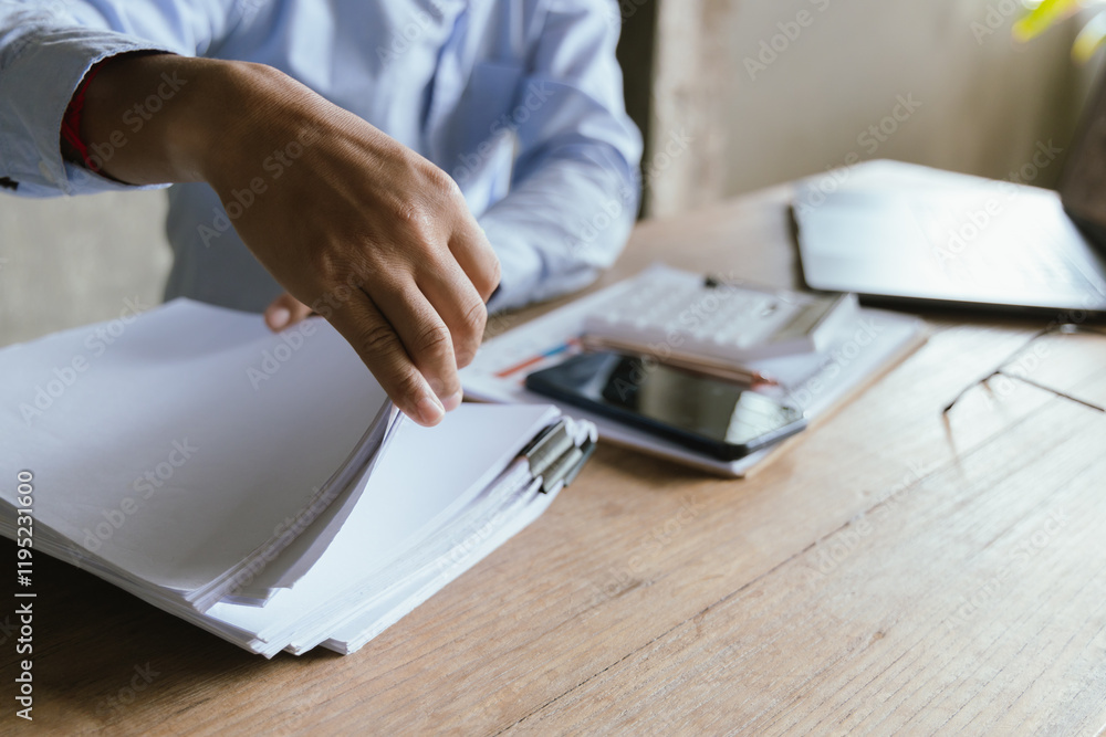 Fototapeta premium A businessman analyzing financial charts and data on a digital tablet in a modern office. Surrounded by reports, graphs, and a laptop, he plans strategies for growth, investment, and corporate success