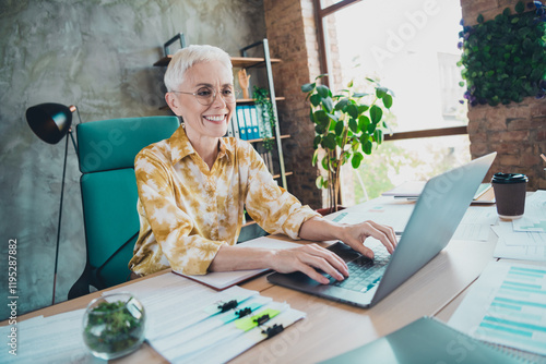 Photo of lovely pensioner lady typing netbook dressed yellow print shirt formalwear comfortable startup office loft room interior photo